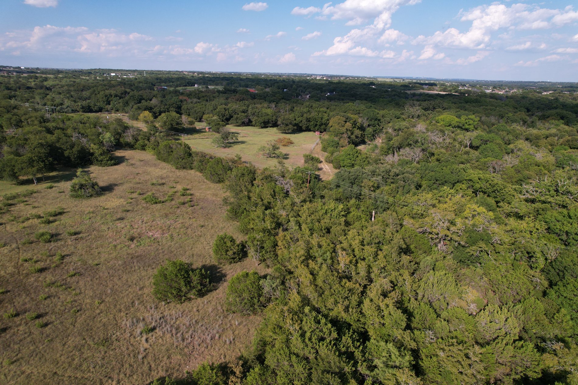 Aerial view of the tract: open ground at the north edge with unbroken tree canopy beyond, and the Fort Worth skyline on the horizon