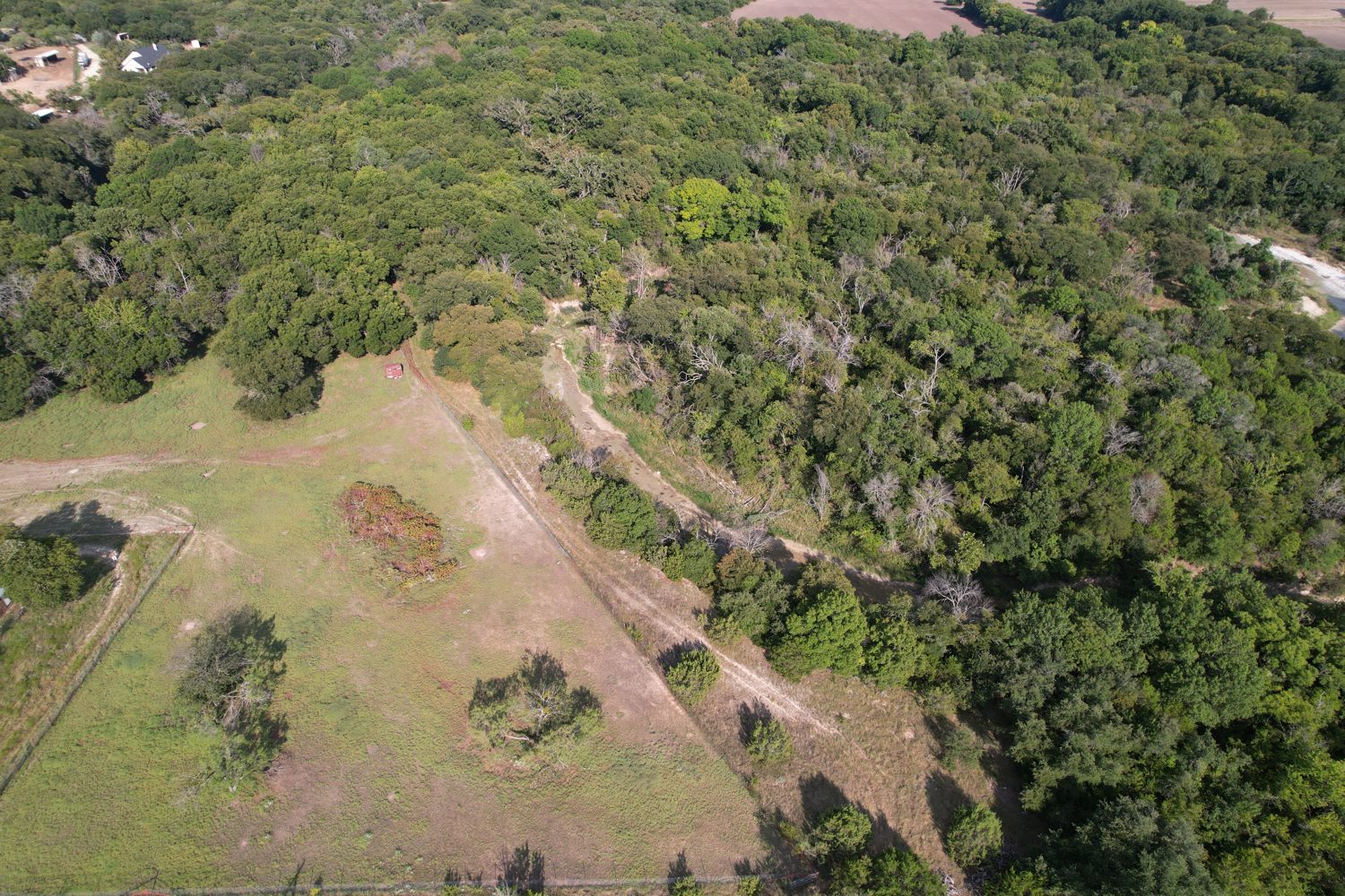 Overhead view of the north clearing with the metal shed, a two-track along the fence line, and the creek channel cutting into the timber